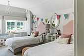 Bunting and pink headboards in sunlit twin room of grade II-listed family home in Godalming Surrey UK