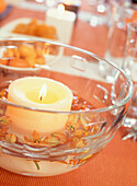 Burning candle in bowl of water with flowers 