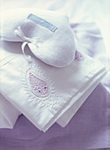 Embroidered bed linen folded in a pile with heart shaped lavender cushion 
