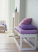 White bench seat with purple cushions in pale blue living room