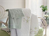 Bed linen draped over the end of a bed in a feminine bedroom with white and green decor
