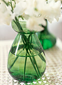 Detail von grüner Glasvase auf Tischplatte mit weißen Schnittblumen