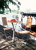 Tischset mit Erdbeeren und Weingläsern für ein romantisches Picknick zu zweit am Fluss mit einem Boot, das nebenan anlegt