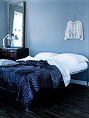 Unmade double bed with satin quilt and lace camisole top and dark wooden floorboards in light blue bedroom