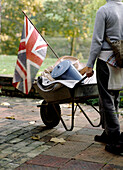 Woman pushing a wheel barrow full of household goods with Union Jack flag flying on the front
