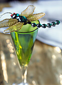 Dragonfly decoration with gold wings and semi precious stones on top of a green stemmed glass