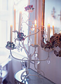 Dekorativer Metallkronleuchter mit geschliffenen Glasanhängern und brennenden Kerzen vor einem Barockspiegel