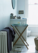 Contemporary bathroom with folding tray table and toiletries radiator with draped towels and white painted floorboards
