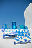 Collection of blue glassware and fabrics hang on whitewashed wall of Greek villa