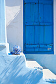 Geblümte Vase auf einer Treppe mit blau gestrichenen Fensterläden im Innenhof einer griechischen Villa