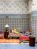 Bunte Stoffe auf einem Tagesbett in einem marokkanischen Riad mit geometrischen Kacheln in Nordafrika