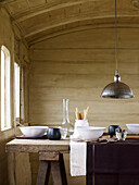 Metal pendant light above trestle with ceramic bowls and glassware