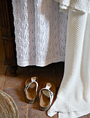 Pair of sandals and white fabrics in bedroom of Sicilian home