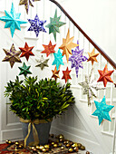 Assorted star decorations on banister with cut leaves in pot and baubles