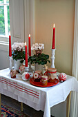 Leuchtend rote Kerzen und hausgemachte Marmelade mit weißen Alpenveilchen auf dem Tisch