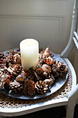 Candle and pine cones on wicker chair seat