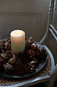 Lit candle and pine cones on wicker chair seat