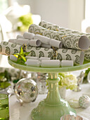 Green and white Christmas crackers on cake stand with baubles