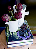 Purple artichoke flowers in vase with necklace and books