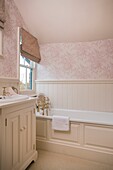 Pink floral patterned wallpaper and roman blinds in panelled bathroom of timber framed cottage, Grafty Green, Kent, England, UK