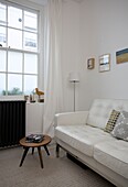 White leather sofa with black radiator below sash window in St Leonards beach house, East Sussex, England, UK
