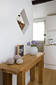 Schnittblumen und Kieselsteine auf einer hellen Holzkonsole in einer weißen Küche in einem Landhaus mit Fachwerk