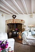 Holzofen und dreiteiliges Sofa im weiß getünchten Wohnzimmer eines Cottage in Corfe Castle, Dorset, England, UK