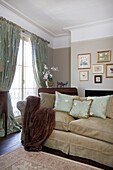 Fur throw on sofa with art display and green silk tie back curtains in Cranbrook home, Kent, England, UK
