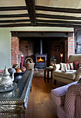 Lit woodburner in brick fireplace in beamed living room in Sandhurst cottage, Kent, England, UK