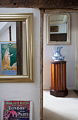 Vintage poster reflected in mirror of hallway with washbowl and jug on plinth in Egerton cottage, Kent, England, UK