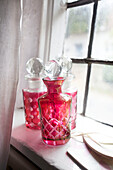 Pink hand coloured decanters on window sill of Egerton cottage, Kent, England, UK