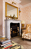 Upholstered armchair at fireplace with gilt framed mirror and wood burning stove in Kent home England UK