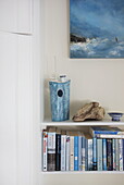 Blaue Bücher und Kunstwerke auf weißen Regalen in einem Haus in Dartmouth, Devon, Vereinigtes Königreich