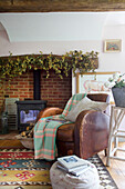 Brown leather sofa at fireside with wood burning stove in High Halden farmhouse Kent England UK