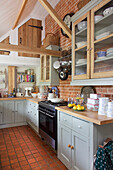 Range oven and glass fronted fitted units in exposed brick kitchen of High Halden farmhouse Kent England UK