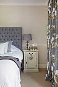 Floral curtains and buttoned headboard with painted bedside cabinet in Staplehurst home Kent England UK