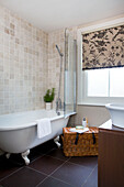 Freestanding bath in cream tiled bathroom with floral roller blind in Staplehurst home Kent England UK