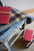 Red hardbacked books with tartan blanket on weathered chair in Kent farmhouse England UK