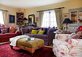 Floral print armchair and purple sofa with ottoman footstool in Kent farmhouse living room England UK