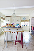 Pink barstool at kitchen island in white fitted kitchen of Bishops Sutton home Alresford Hampshire England UK