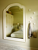 White mirror frame reflecting bedroom with hooks in Kensington home London England UK