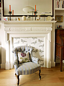 Upholstered armchair and cushion in front of fireplace with ornaments in London home England UK