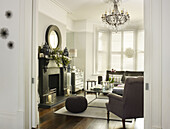 Grey armchair at fireplace with wicker stool below chandelier in living room of London home England UK