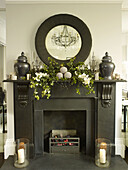 Weihnachtsgirlanden auf schwarzem Kamin mit rundem Spiegel und Urnen in einem Haus in London, England, UK
