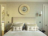 Buttoned cushions on double bed with circular mirror on patterned wallpaper in bedroom of London home England UK