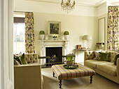 Checked ottoman and sofas with floral patterned curtains in living room of East Sussex country house England UK