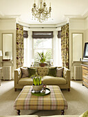 Checked ottoman with sofa and floral patterned curtains at bay window in East Sussex country house England UK