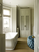 Freestanding bath with blue buttoned seat at window in East Sussex country house England UK