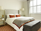 Light grey headboard with burnt ochre velvet cushions and blanket trim in bedroom of North London townhouse England UK