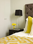 Black lamp on side table with geometric bed cover and buttoned headboard in Little Venice townhouse London England UK